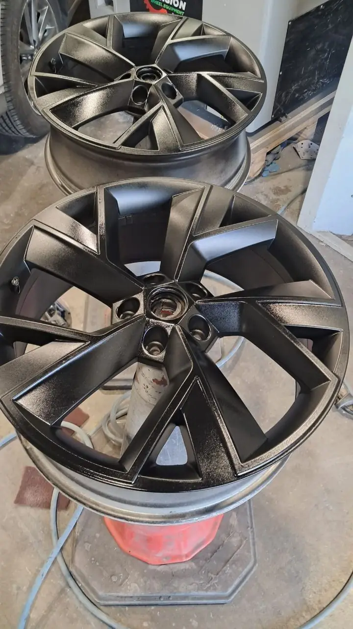 Two alloy wheels on stands in the workshop, freshly sprayed matt black