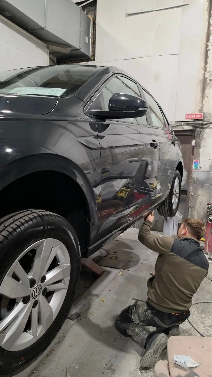 Technician checking the sill of a grey Volkswagen raised on the workshop ramp