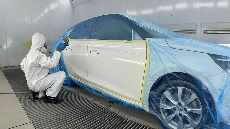 Painter spraying white car doors in the spray booth